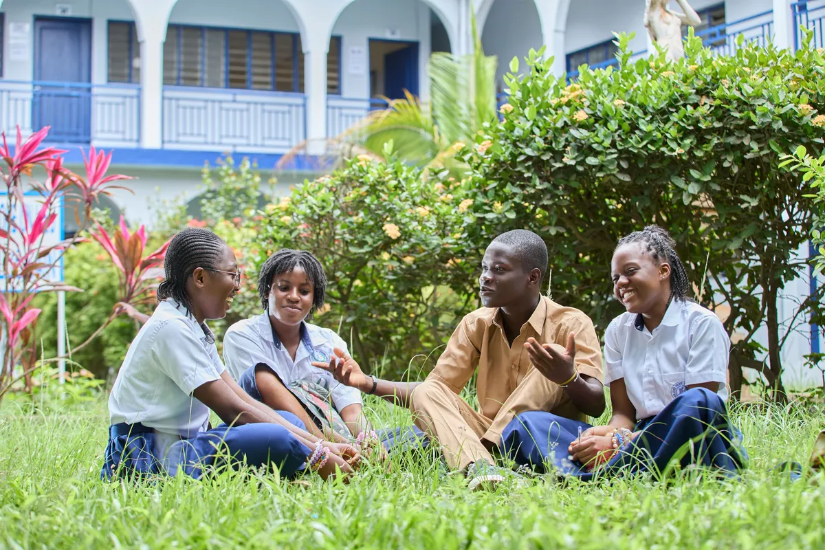 Students in uniform talking with their teacher on the school lawn