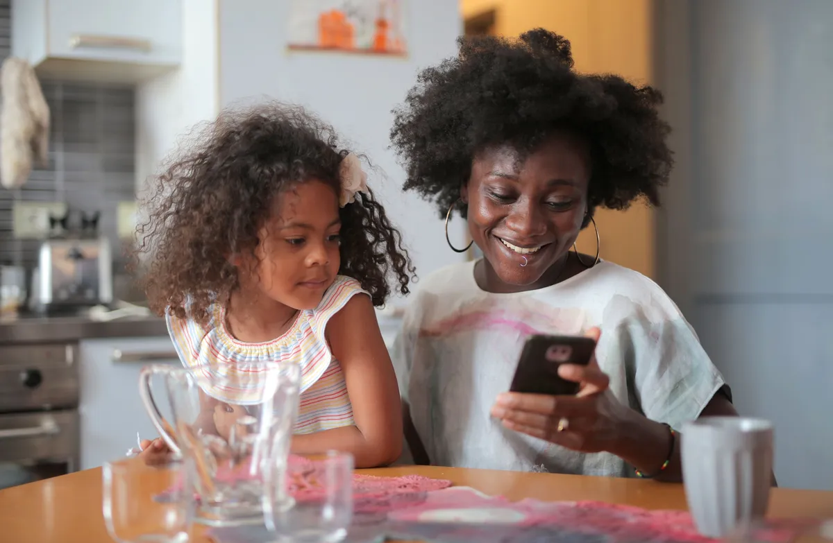 A parent and child looking at a phone together at the kitchen table